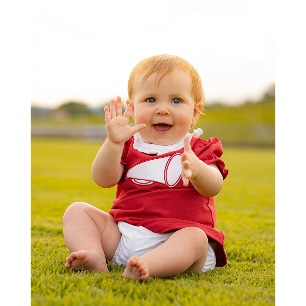 That Store burgundy cotton bloomer set with megaphone applique worn by a happy baby girl sitting on green grass