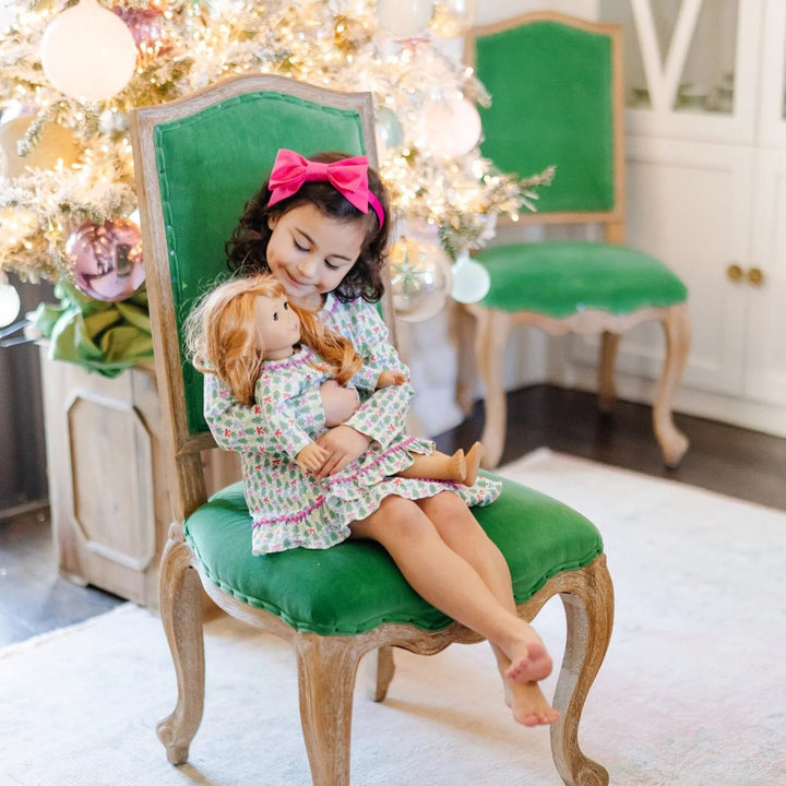 That Store Carlin doll dress in tree topper bows print with pom-pom trim, worn by a girl holding a matching doll.
