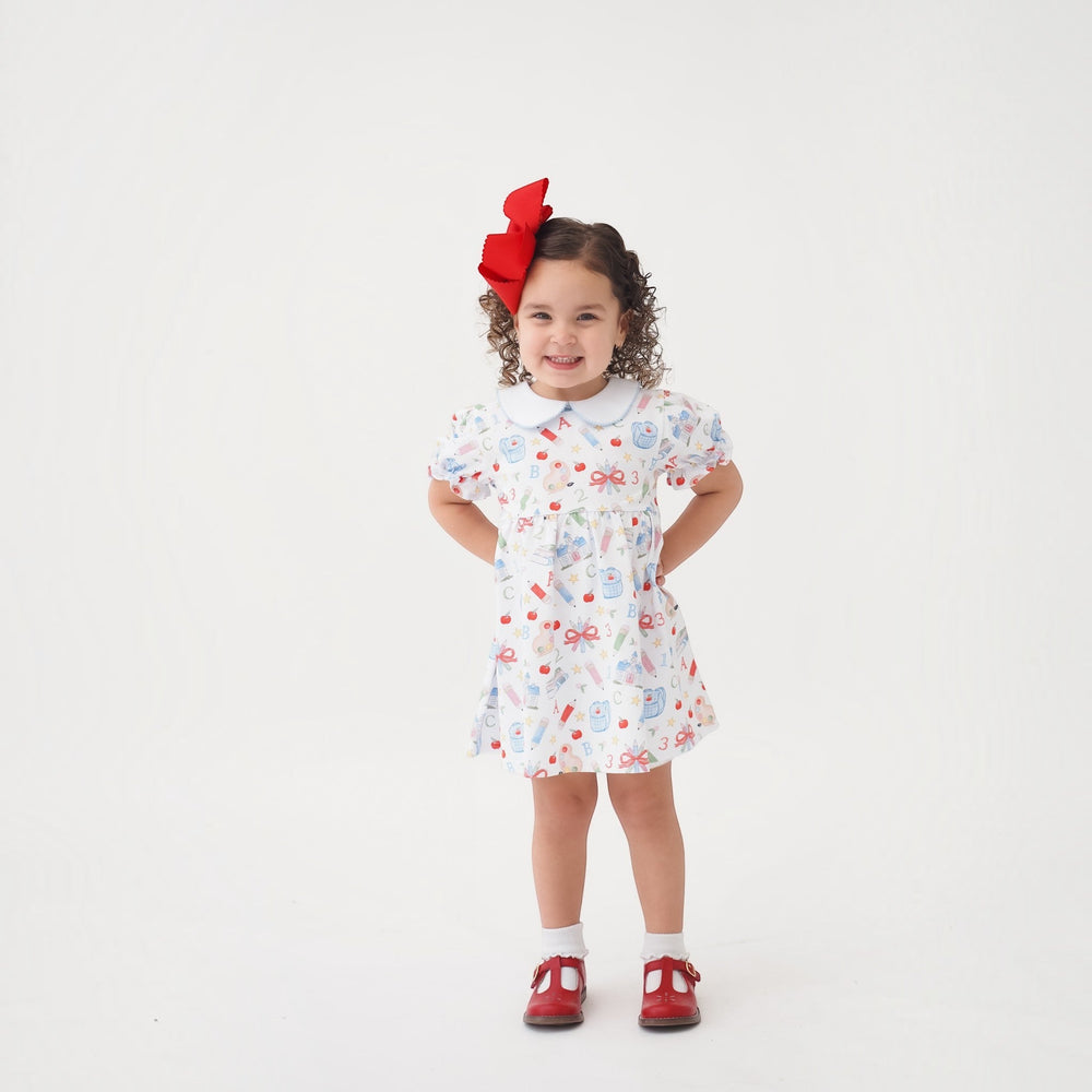 That Store Collins red classic dress with school supplies print on a smiling girl with a large red hair bow
