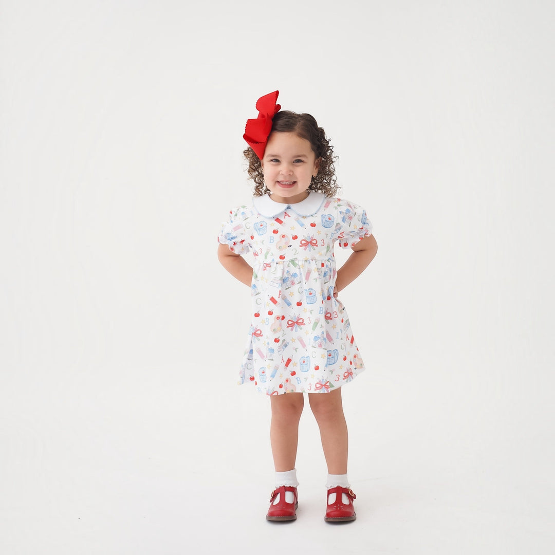 That Store Collins red classic dress with school supplies print on a smiling girl with a large red hair bow