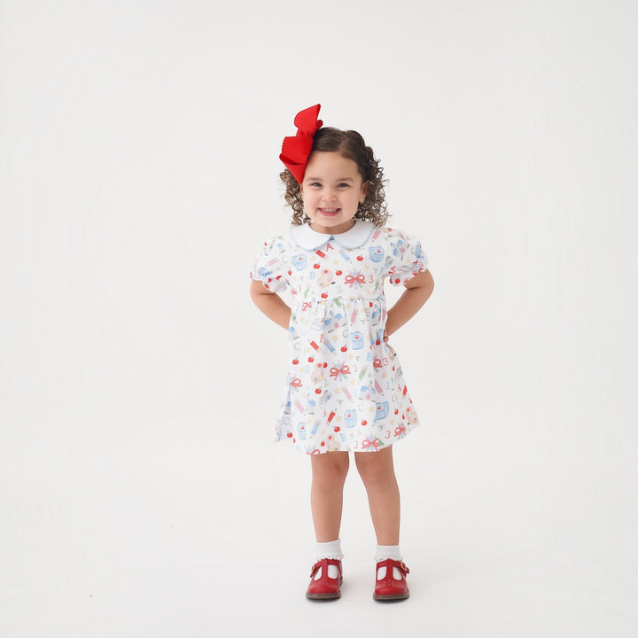 That Store Collins red classic dress with school supplies print on a smiling girl with a large red hair bow