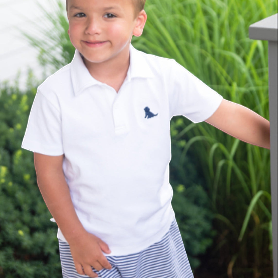 Young boy wearing That Store navy and white striped Conrad knit shorts and a white polo shirt outdoors.
