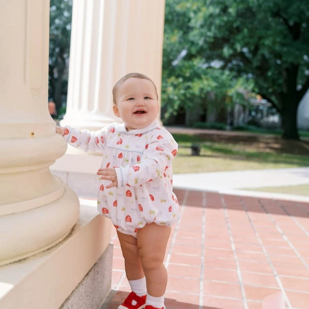 That Store Covington bubble in white knit with Barnyard Tales print, long sleeves, and light blue piping on a baby.