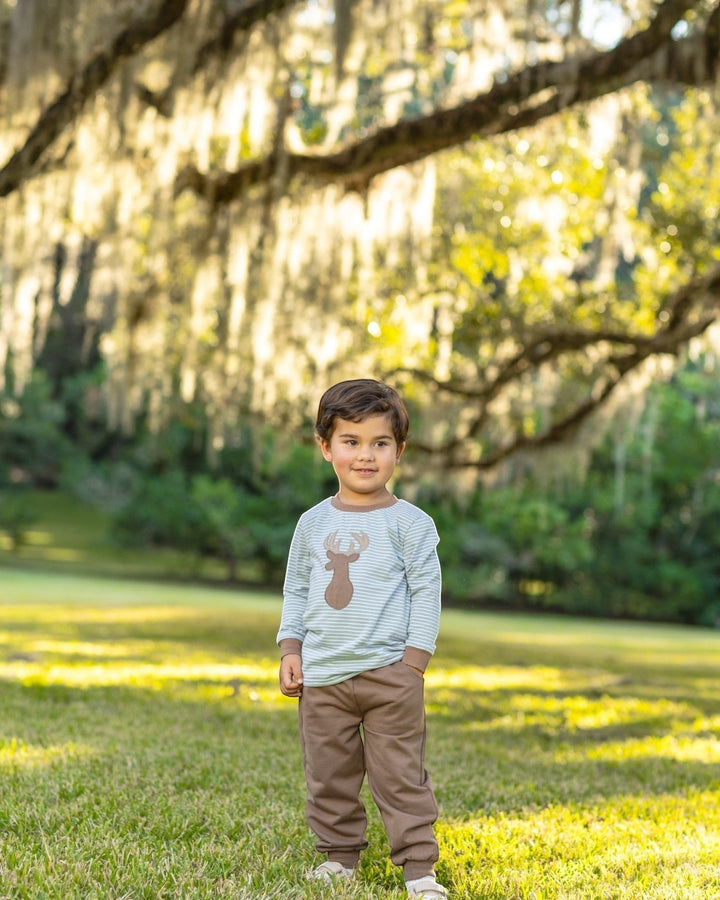 That Store boy wearing a green striped long-sleeve shirt with a deer applique and brown jogger pants in a park.