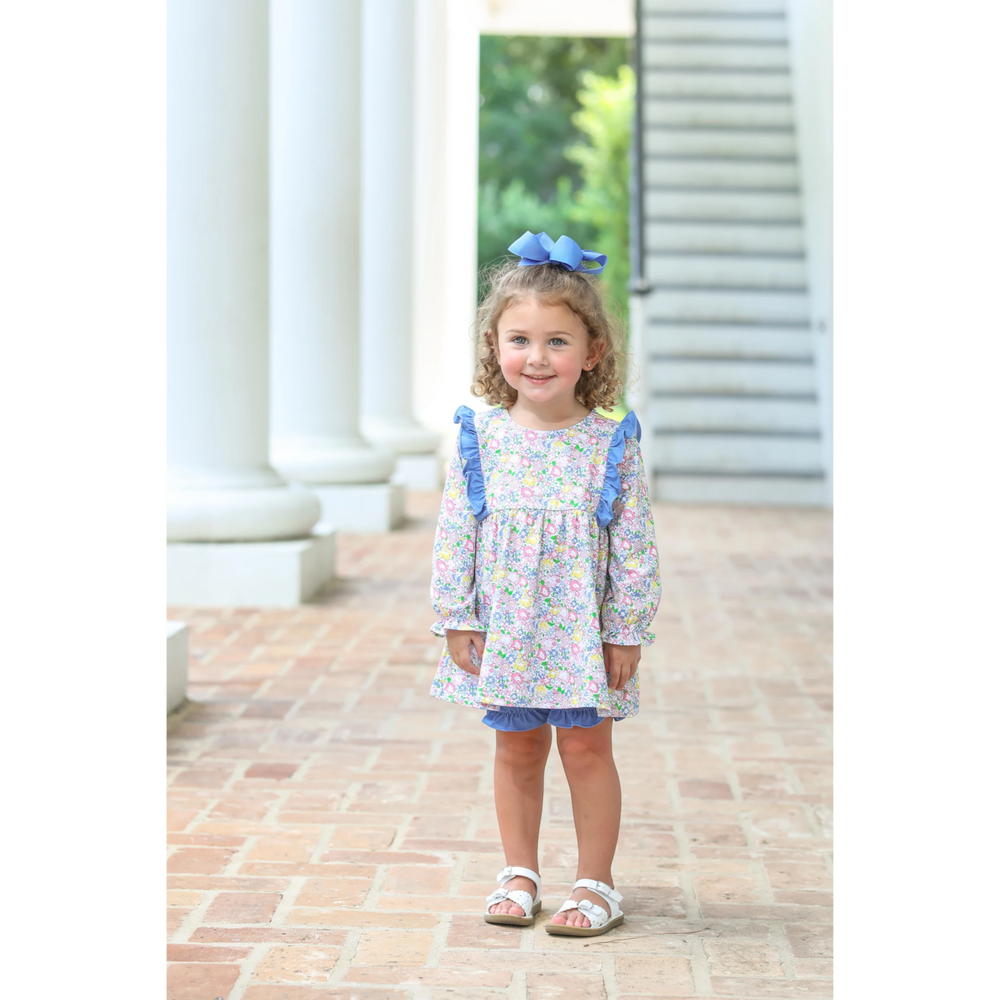 Toddler girl wearing a That Store floral long-sleeve top with blue ruffles and matching bloomers with a blue hair bow