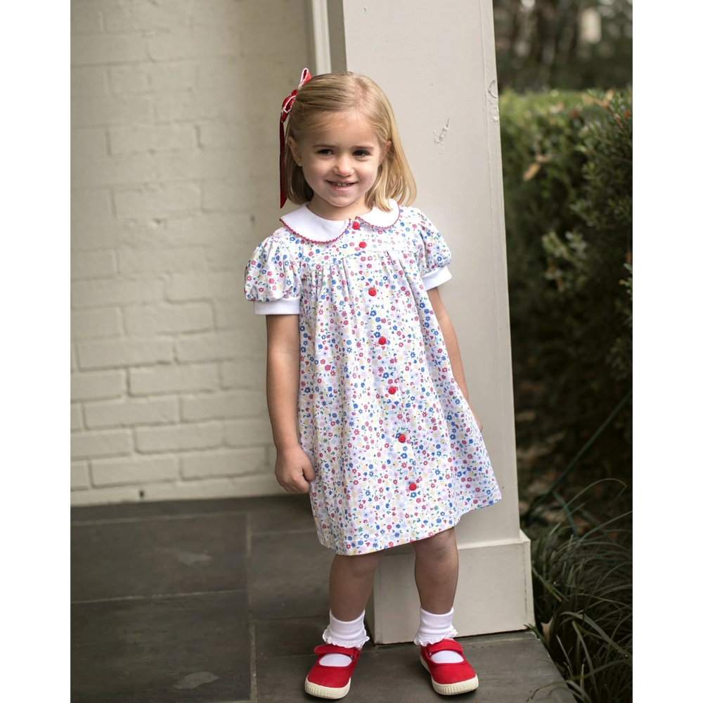 That Store floral dress with red picot trim and buttons worn by a young girl with a red hair bow and red shoes.