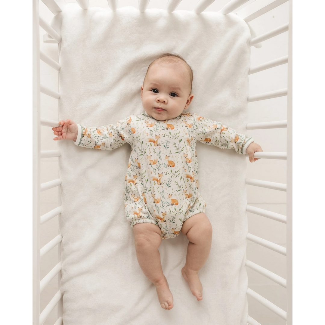 Baby lying in a white crib wearing a That Store long sleeve bubble with a woodland fox and leaf print in Pima cotton.