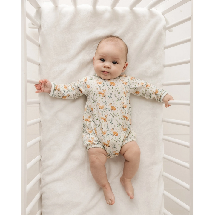 Baby lying in a white crib wearing a That Store long sleeve bubble with a woodland fox and leaf print in Pima cotton.