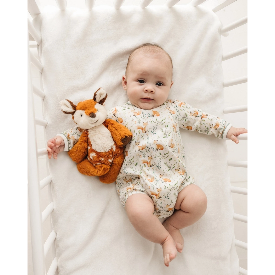 Baby wearing a That Store Fox Tales long sleeve Pima cotton bubble with a plush fox toy in a white crib