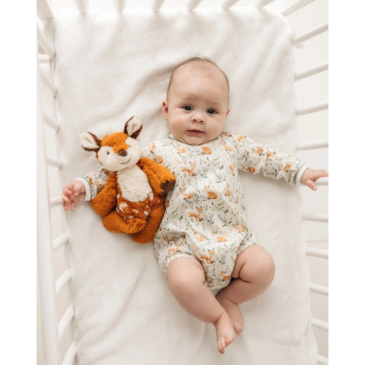 Baby wearing a That Store Fox Tales long sleeve Pima cotton bubble with a plush fox toy in a white crib