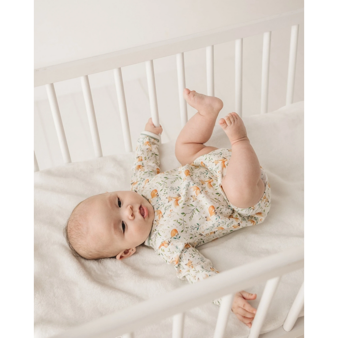Baby wearing a That Store Fox Tales long sleeve Pima cotton bubble with woodland print, lying in a white crib.