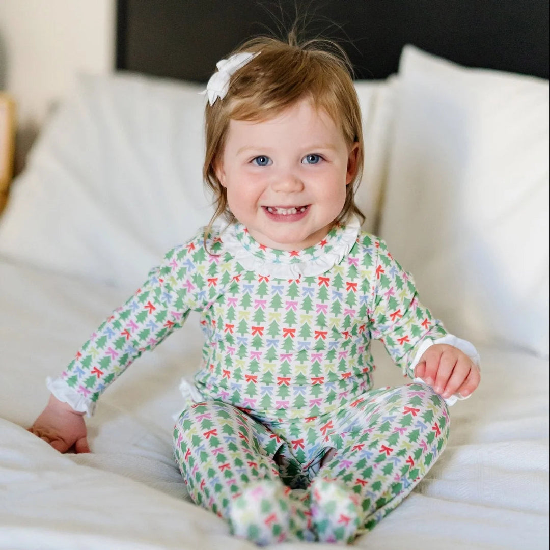 Toddler girl wearing a That Store long-sleeve footed romper with a green Christmas tree and colorful bow print.