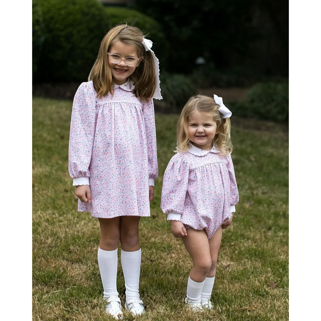 Two girls wearing That Store Pumpkin Grove floral dresses with white collars and bows standing on a grassy lawn.