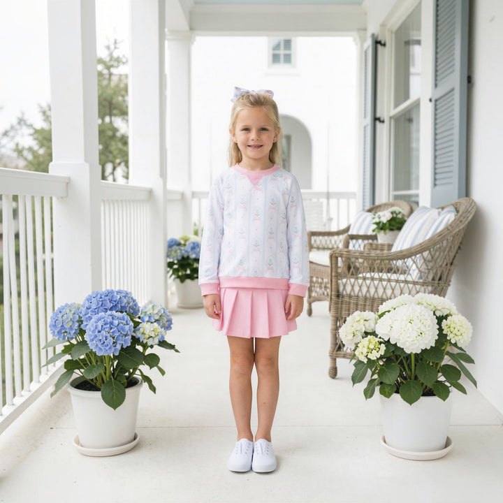 Young girl wearing a That Store pink and white cameo print pullover and matching pleated skirt on a porch.