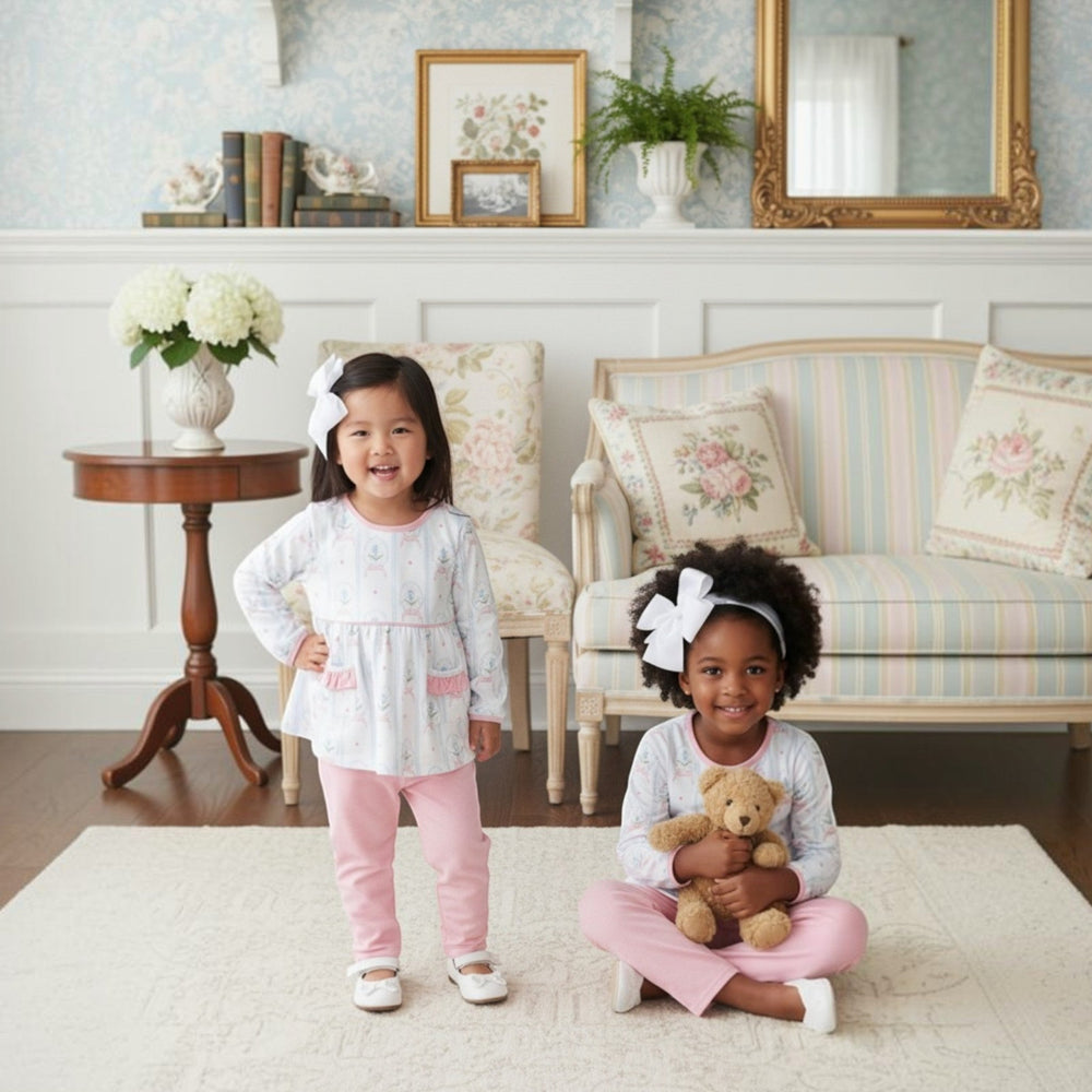 Two girls wearing That Store pink floral rose cameo legging sets with white bows in a cozy living room setting.