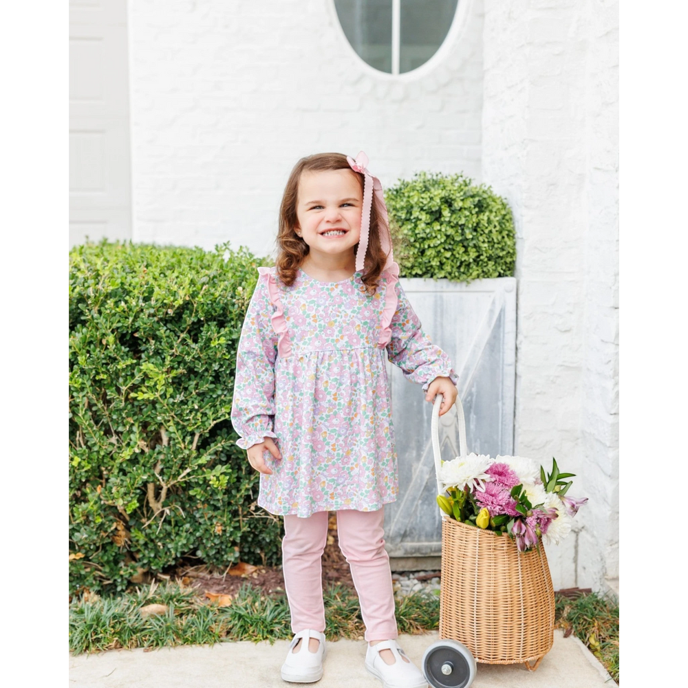 A young girl wearing a That Store pink floral long-sleeve tunic and matching leggings, holding a basket of flowers.