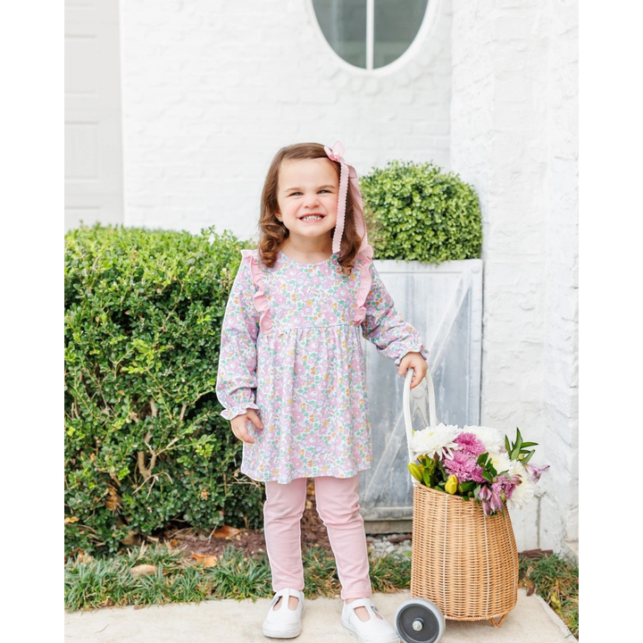 A young girl wearing a That Store pink floral long-sleeve tunic and matching leggings, holding a basket of flowers.