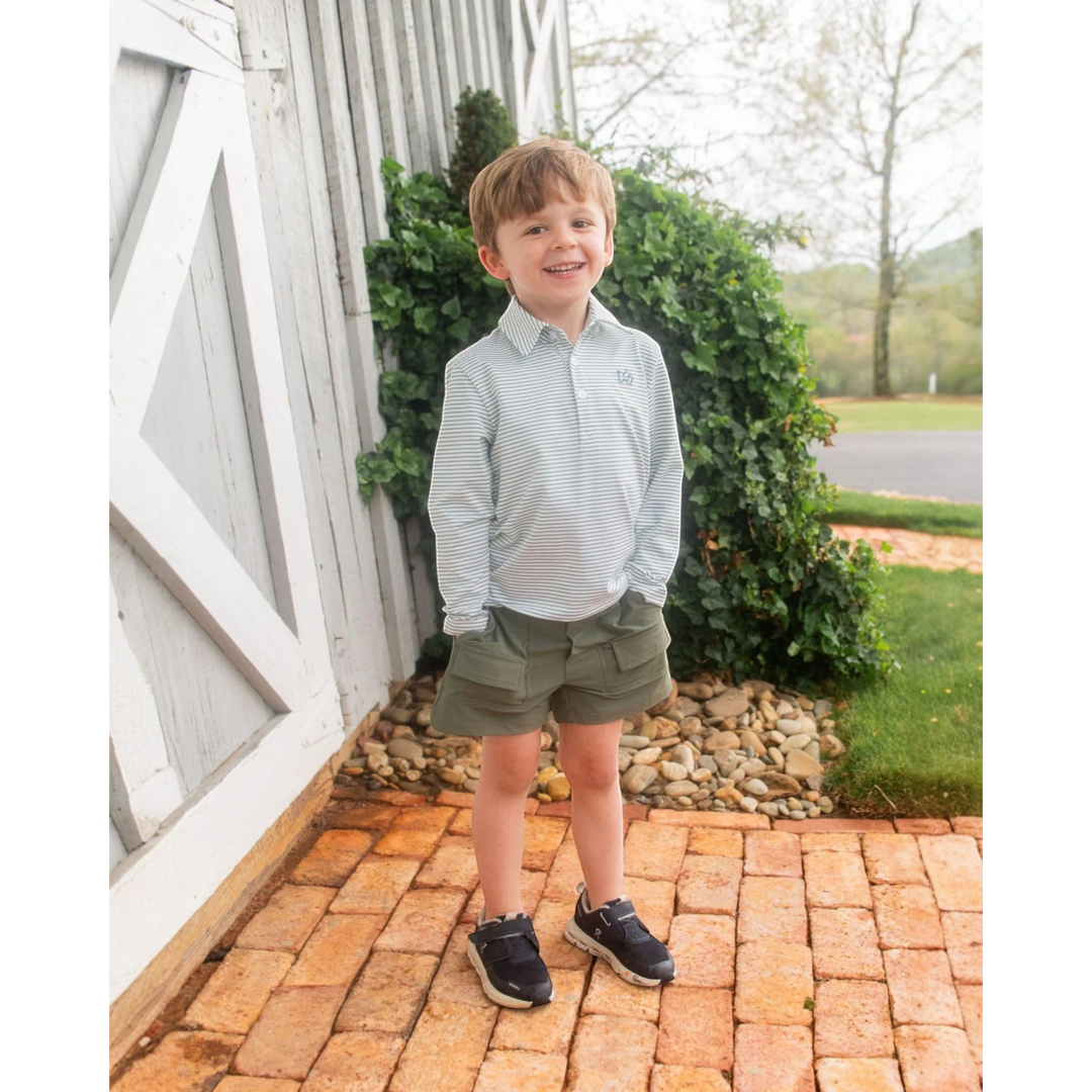 A young boy wearing a That Store green spruce striped long sleeve performance polo shirt with olive green shorts.