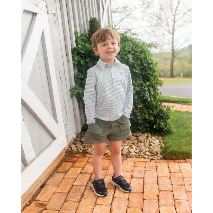 A young boy wearing a That Store green spruce striped long sleeve performance polo shirt with olive green shorts.