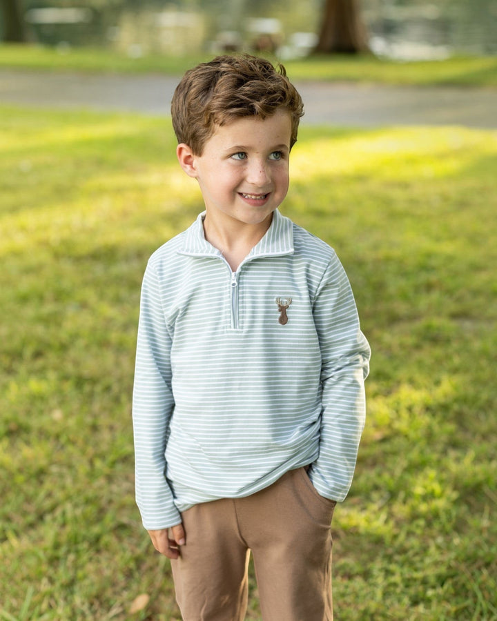 Young boy wearing a That Store green and white striped quarter-zip pullover with a deer motif on a grassy lawn.