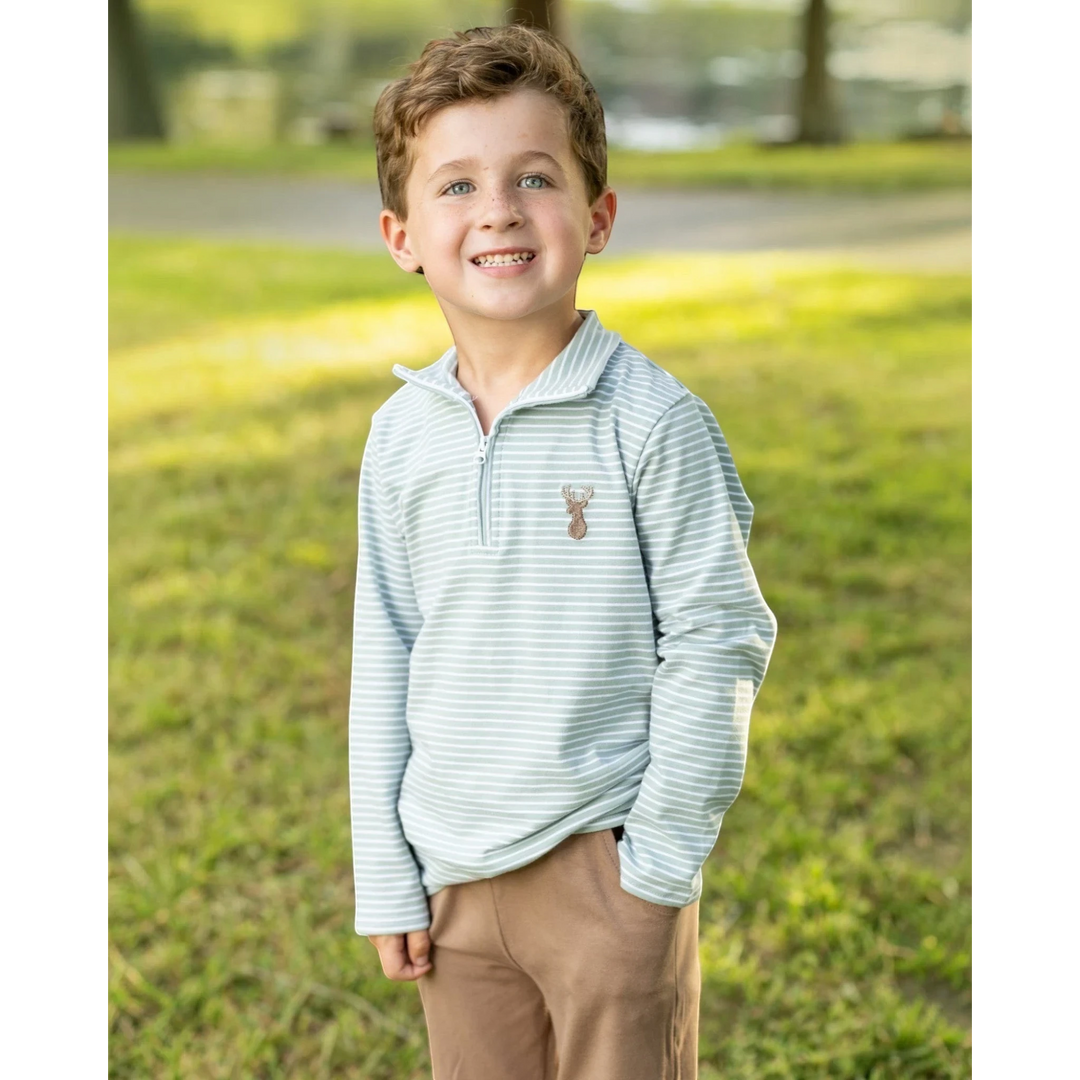 Young boy wearing a That Store green striped quarter-zip pullover with a deer motif, standing in a sunny park.