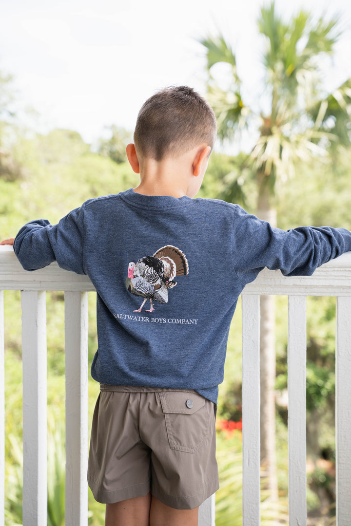Young boy wearing a That Store heather blue long sleeve tee with a turkey graphic on the back, outdoors.
