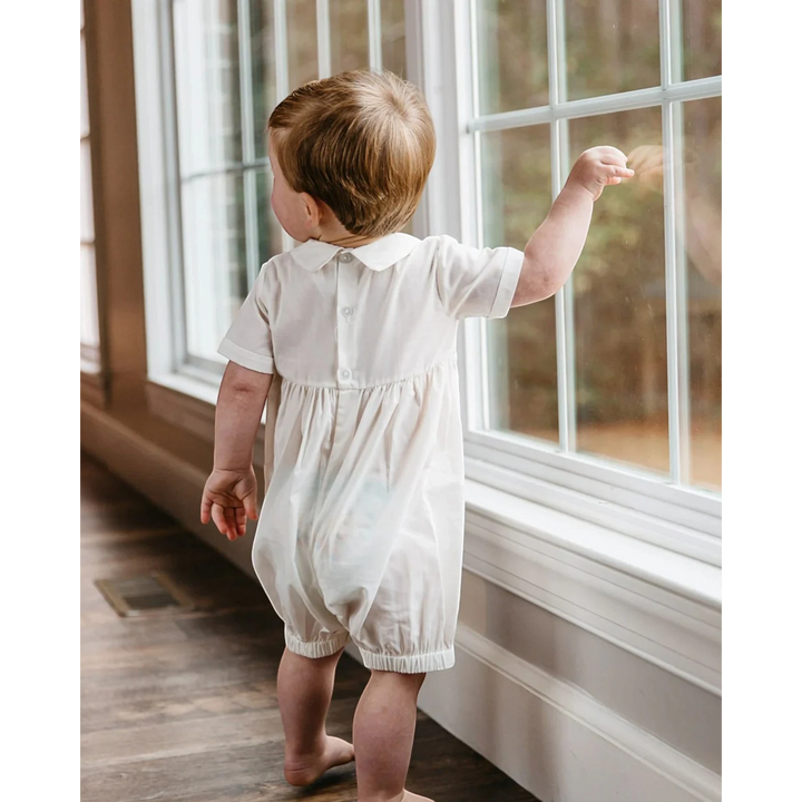 That Store ivory vintage smocked baby boy romper with French lace collar, viewed from the back by a window.