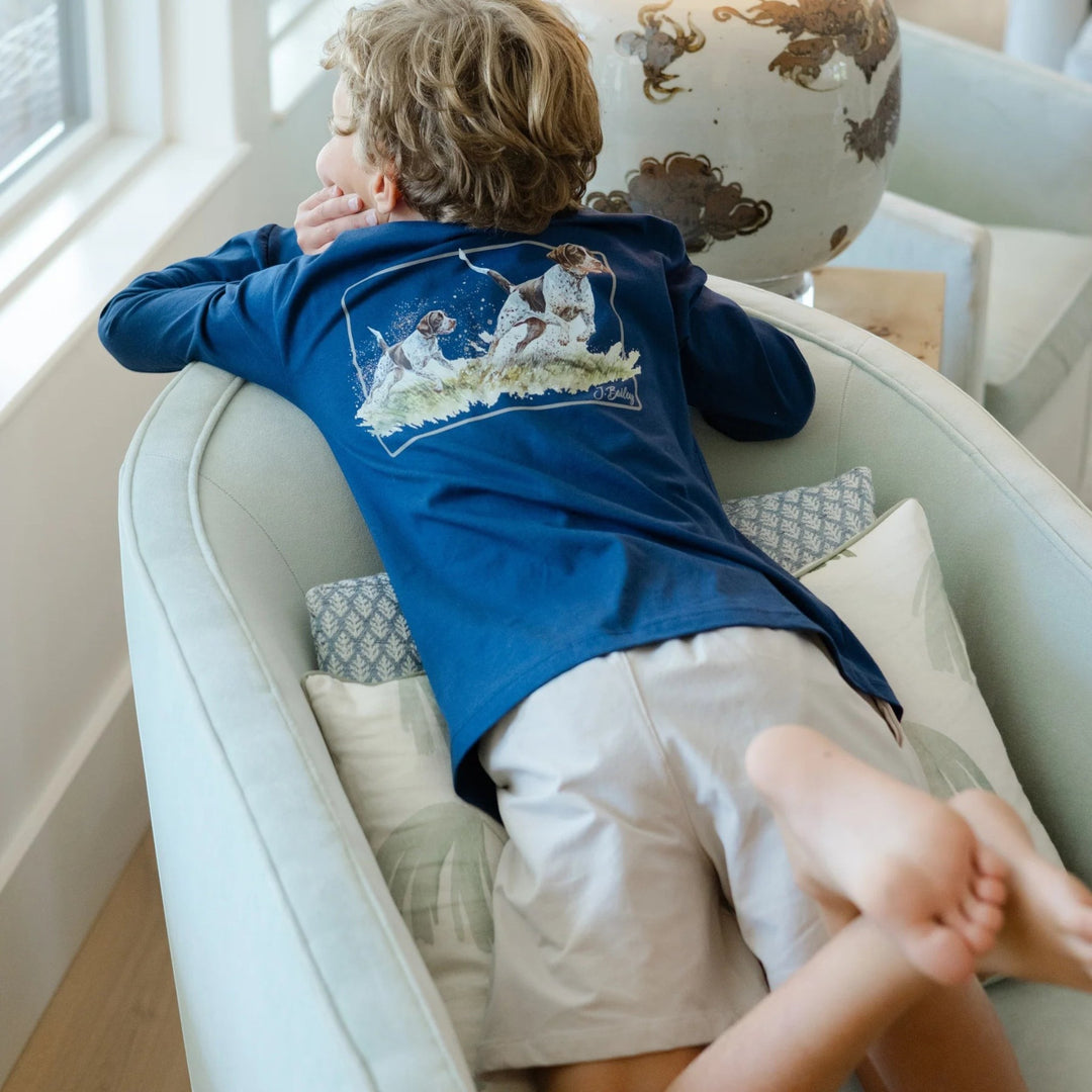 That Store khaki performance shorts on a boy wearing a navy long-sleeve shirt, sitting in a chair by a window.