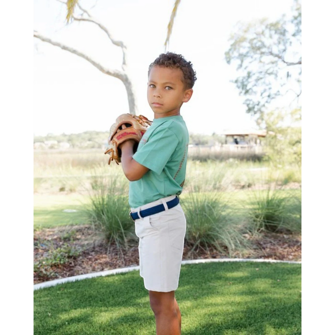 A young boy wearing That Store khaki performance shorts with a navy belt, holding a baseball glove outdoors.