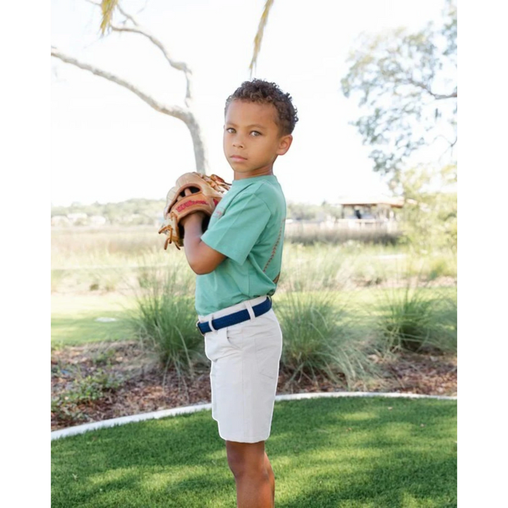 A young boy wearing That Store khaki performance shorts with a navy belt, holding a baseball glove outdoors.
