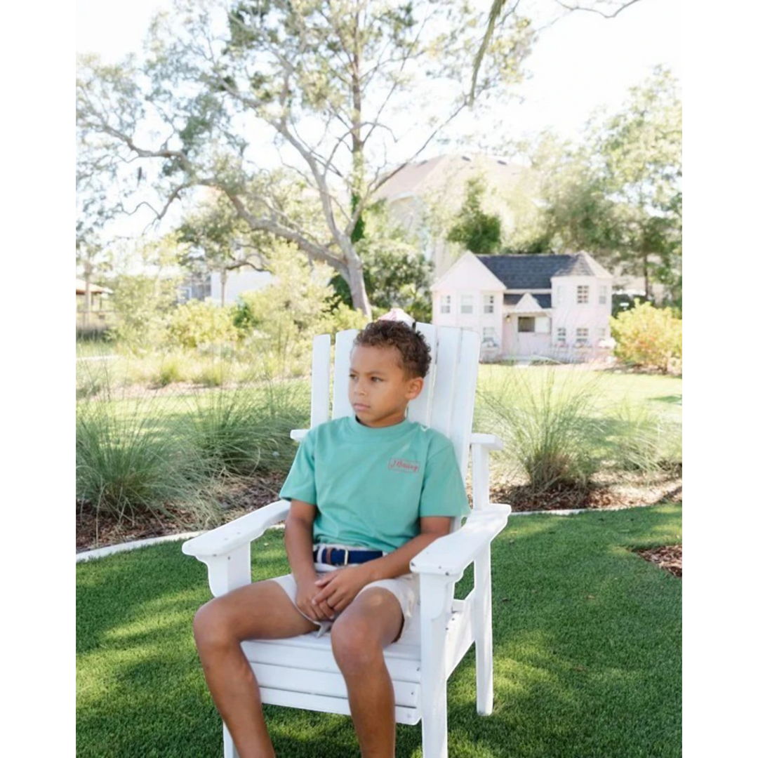 Young boy wearing That Store khaki performance shorts and a green t-shirt sitting in a white chair outdoors