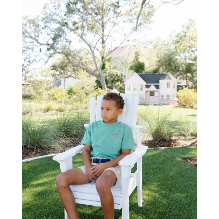 Young boy wearing That Store khaki performance shorts and a green t-shirt sitting in a white chair outdoors