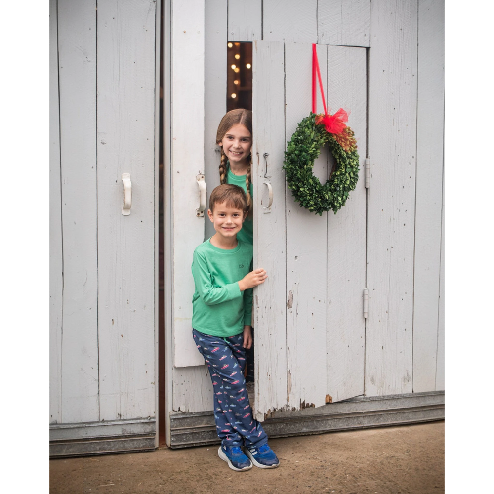 That Store kids lounge pants in blue with festive holiday print worn by a boy standing in a rustic doorway