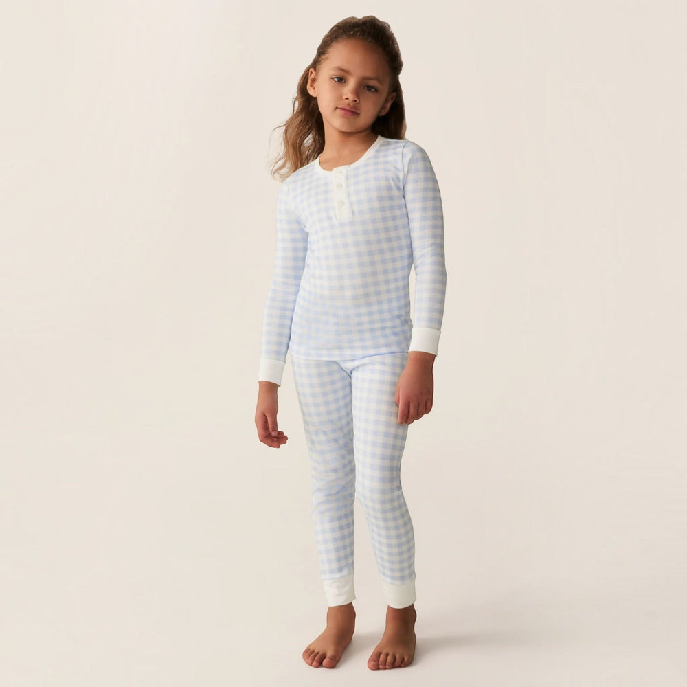 A young girl wearing a That Store light blue gingham pima cotton long sleeve pajama set with a snug fit.