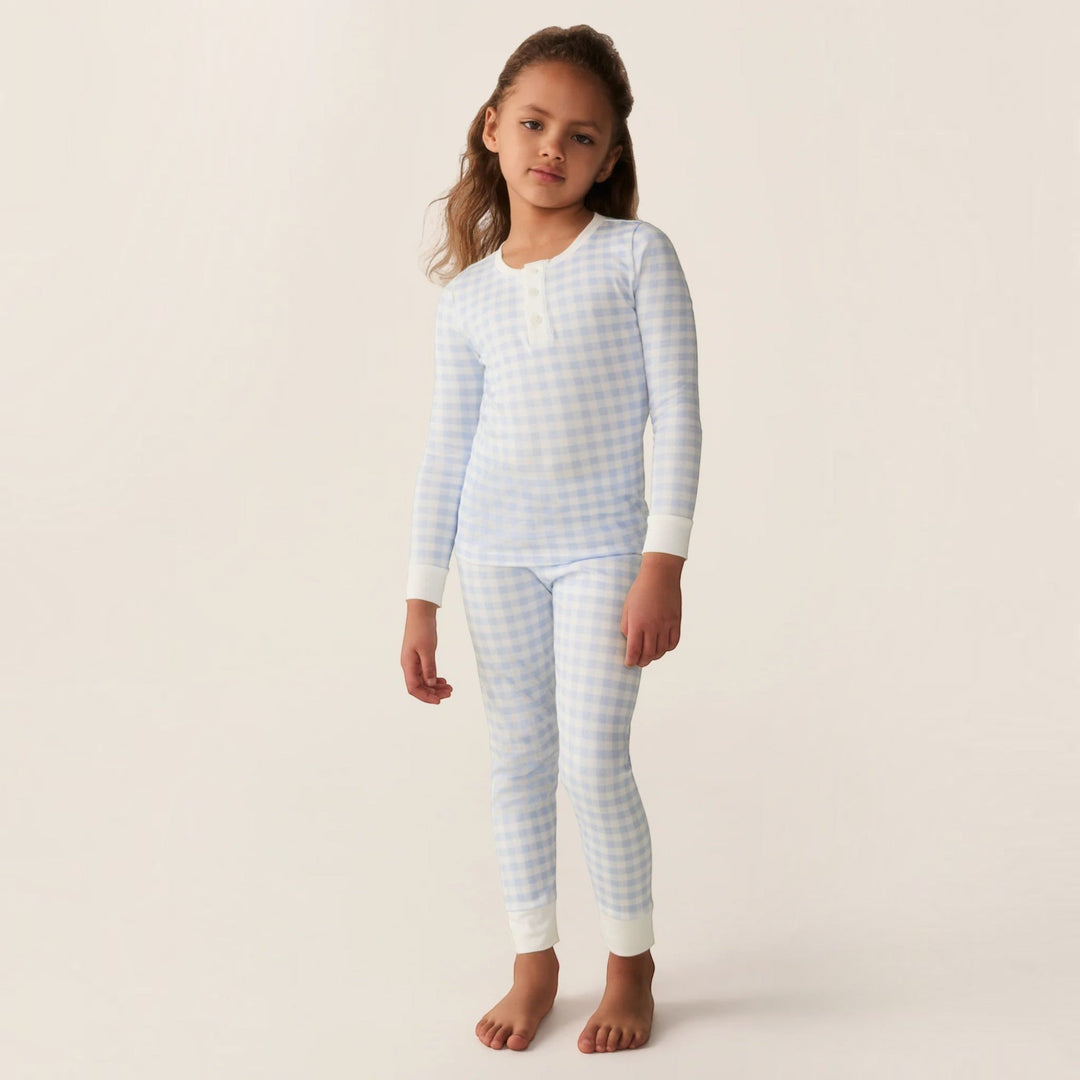 A young girl wearing a That Store light blue gingham Pima cotton long sleeve pajama set with a snug fit.