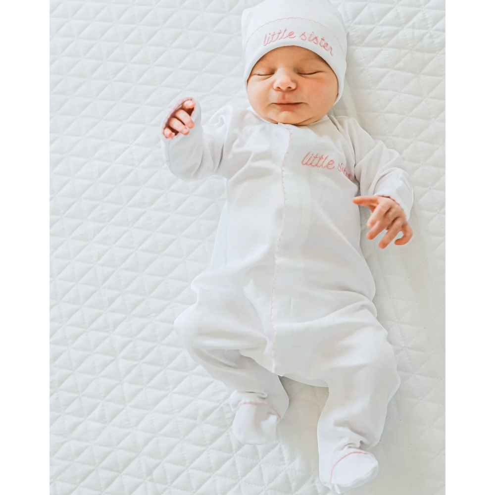 Newborn baby wearing a That Store white pima cotton footie and matching hat with pink Little Sister embroidery.