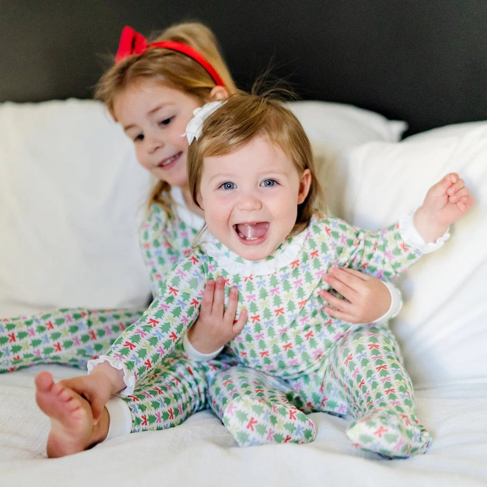 Two girls wearing That Store Lucy footed rompers with green Christmas tree and colorful bow print on white cotton