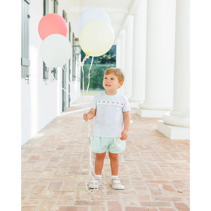 Toddler boy wearing a That Store light blue gingham short set with Mickey balloon embroidery holding colorful balloons
