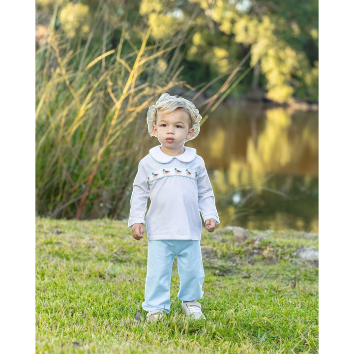 That Store toddler boy wearing a white long-sleeve top with mallard duck embroidery and light blue pants outdoors.