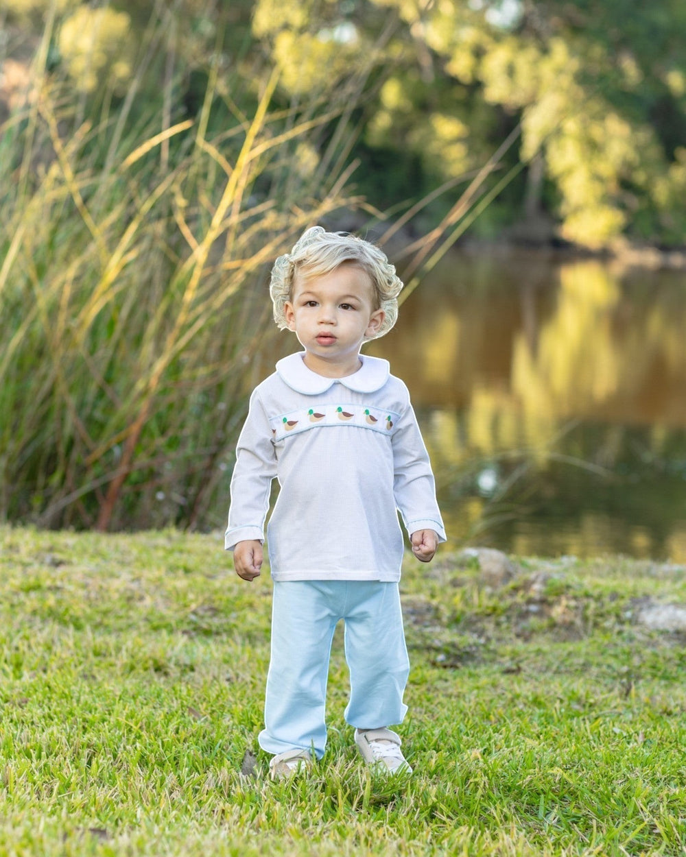 That Store toddler boy wearing a white long-sleeve top with mallard duck embroidery and light blue bloomer pants.