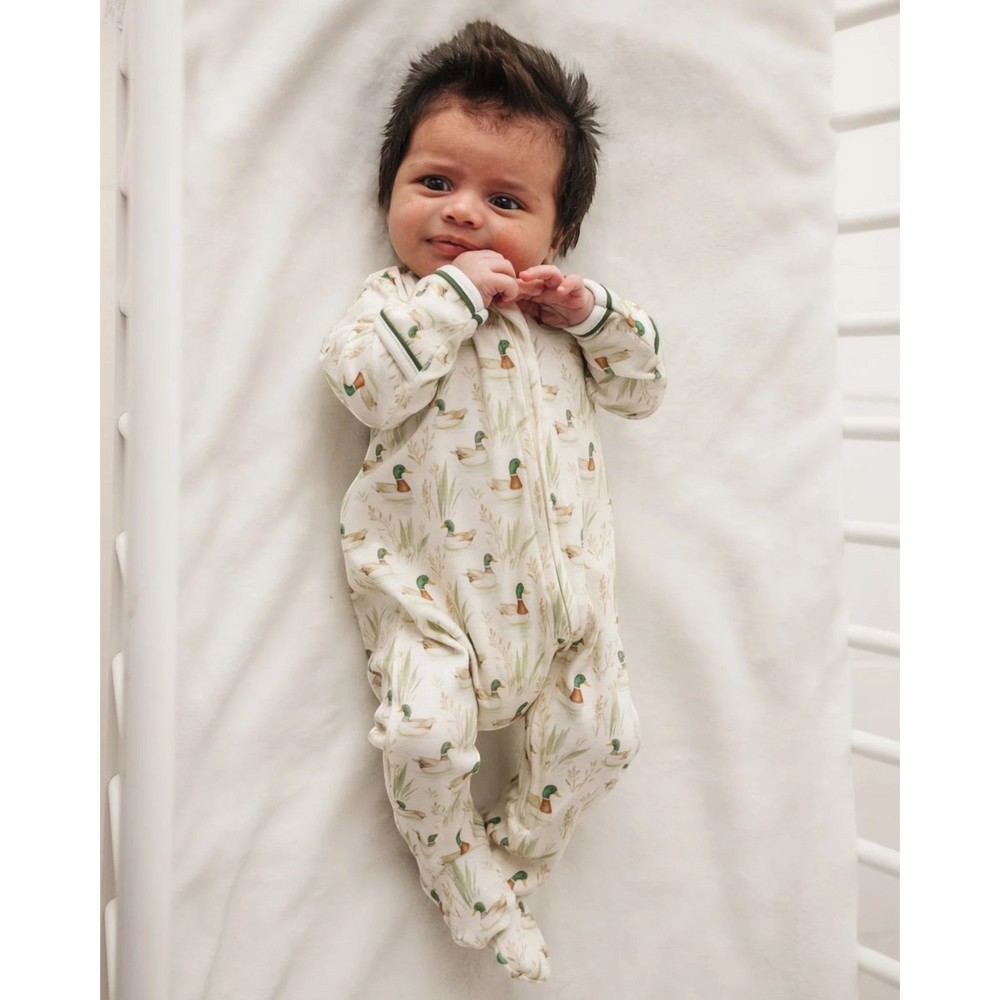 Baby wearing a That Store Mallard's Pond print zip footie made of soft Peruvian Pima cotton in a white crib.