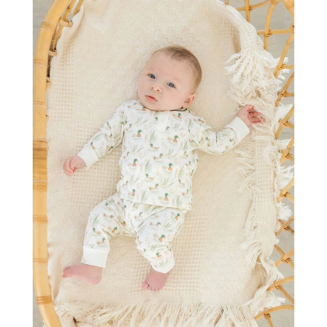 Baby wearing a That Store Mallard's Pond print 2-piece pant set in soft Peruvian Pima cotton, lying in a rattan bassinet.