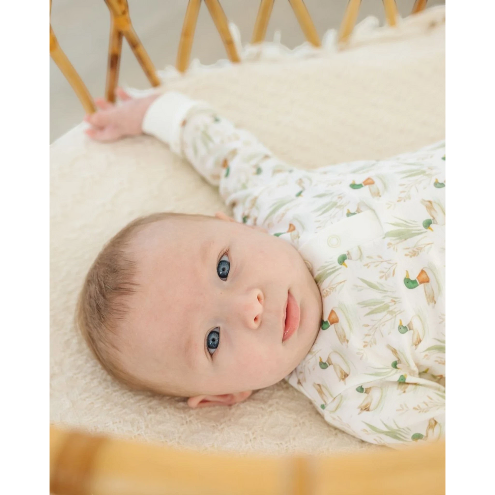 Baby wearing a That Store Mallard's Pond print Pima cotton long-sleeve top while lying in a wicker bassinet.