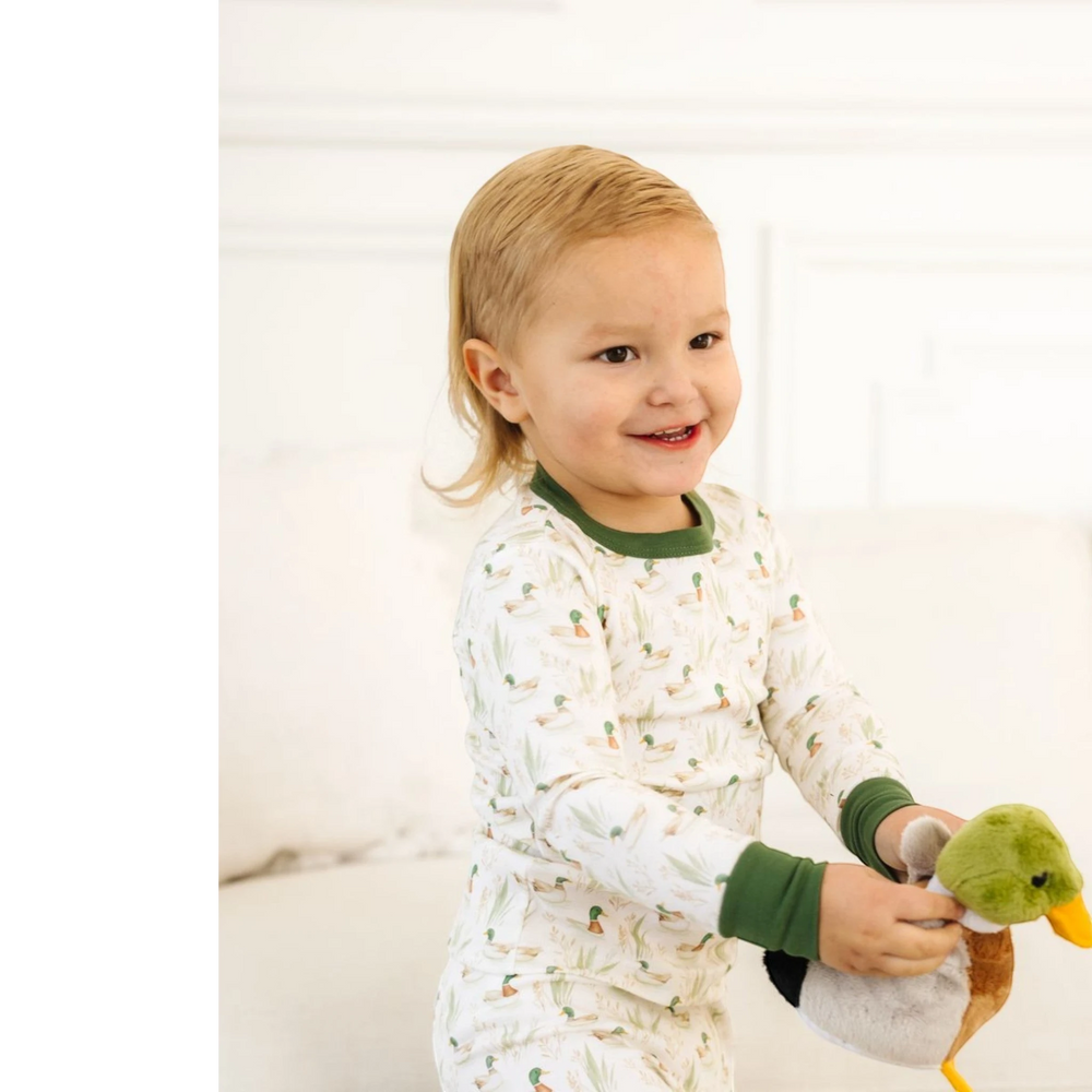Toddler wearing That Store Mallard's Pond green Pima cotton long pajamas while holding a plush duck toy