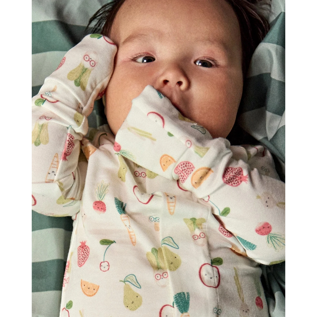Baby wearing a That Store modal convertible coverall with a colorful fruit and vegetable print and mitten cuffs.