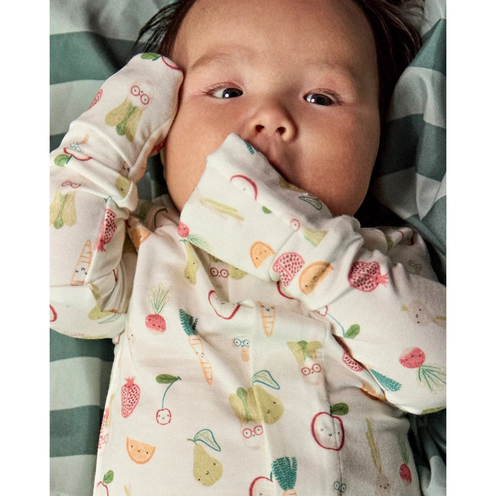 Baby wearing a That Store modal convertible coverall with a colorful fruit and vegetable print and mitten cuffs.