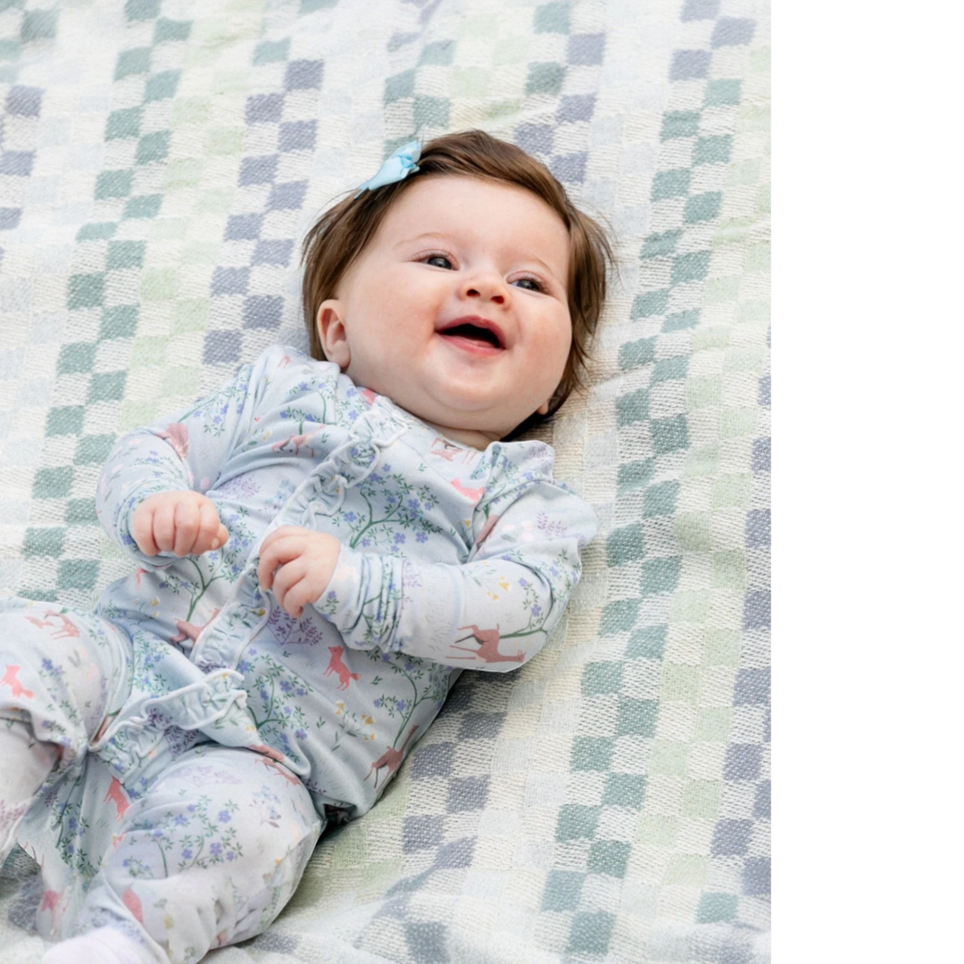 That Store baby girl wearing a soft modal footie with a deer and floral print, featuring ruffle details and magnets.