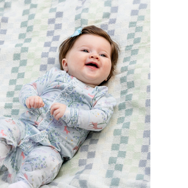 That Store baby girl wearing a soft modal footie with a deer and floral print, featuring ruffle details and magnets.