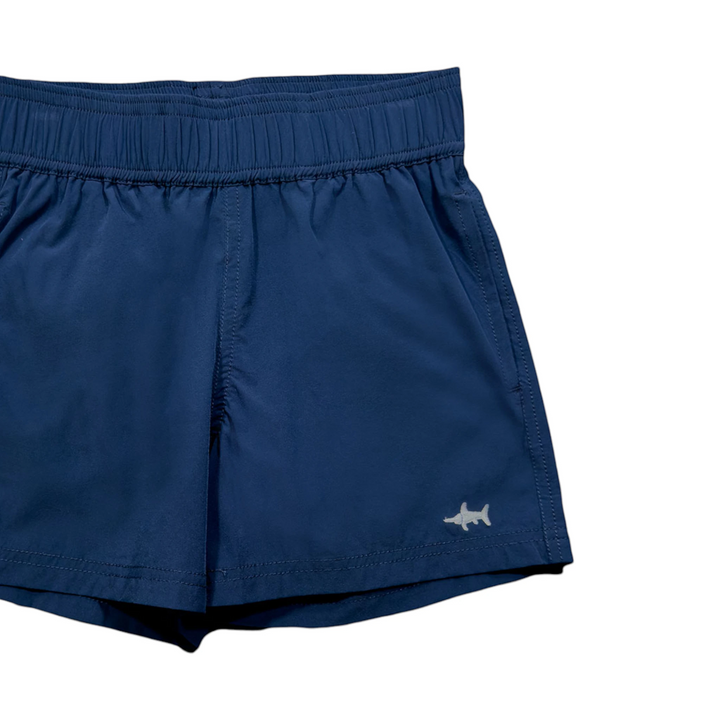 That Store navy boys performance shorts with elastic waistband, moisture-wicking fabric, and small shark logo detail.