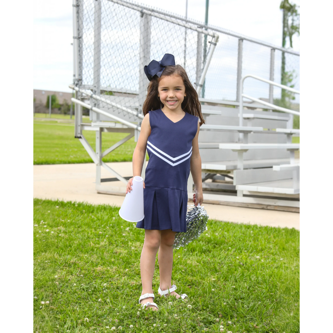 Young girl wearing a That Store navy cheer uniform dress with white stripes, holding a megaphone and silver pom-poms.